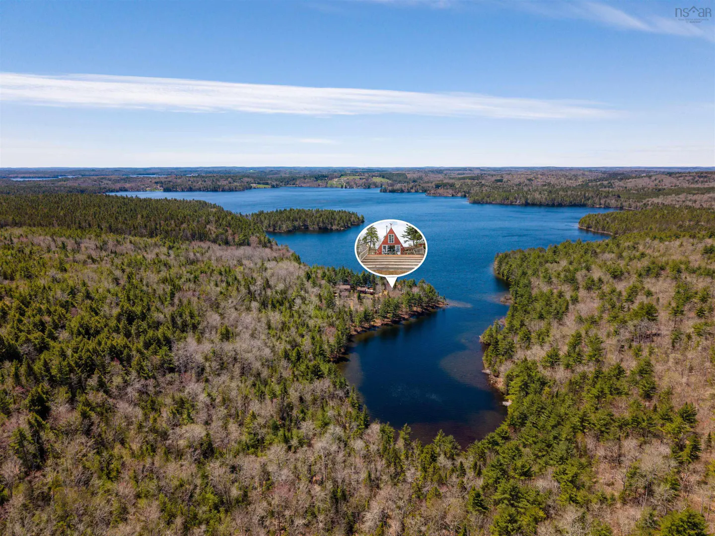 Aerial view of a lake surrounded by forest, with a red house highlighted in a speech bubble.