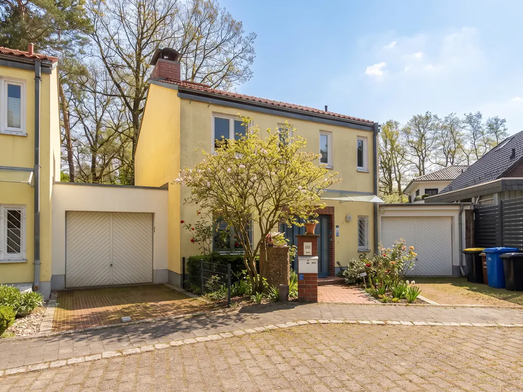 Two-story yellow house with a garage and a tree in front. Brick walkway and driveway. Blue sky.