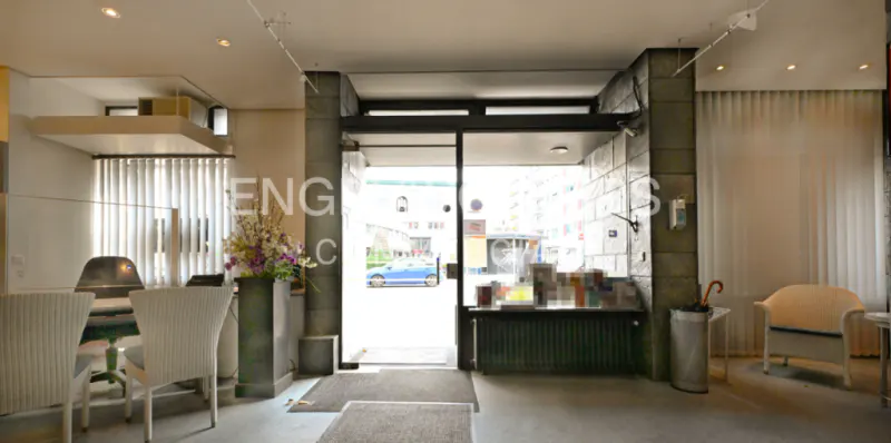 Interior view of a modern office space with a reception desk, white chairs, and an open glass door leading to a street view.