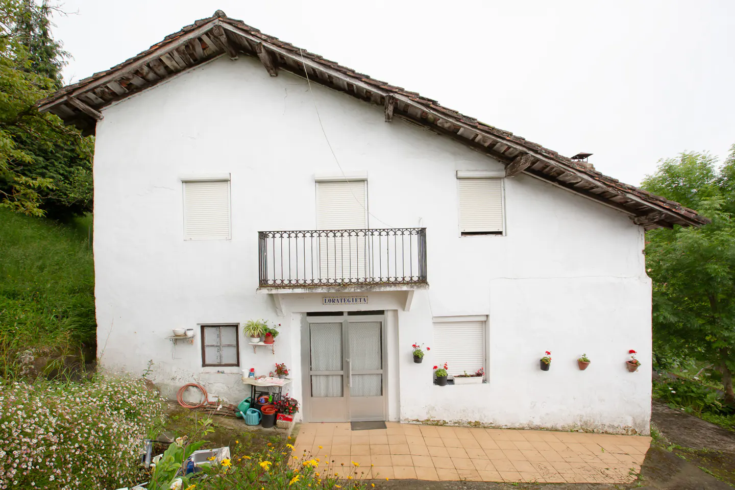Exterior of a white two-story house with a brown roof, a balcony, and flower pots.