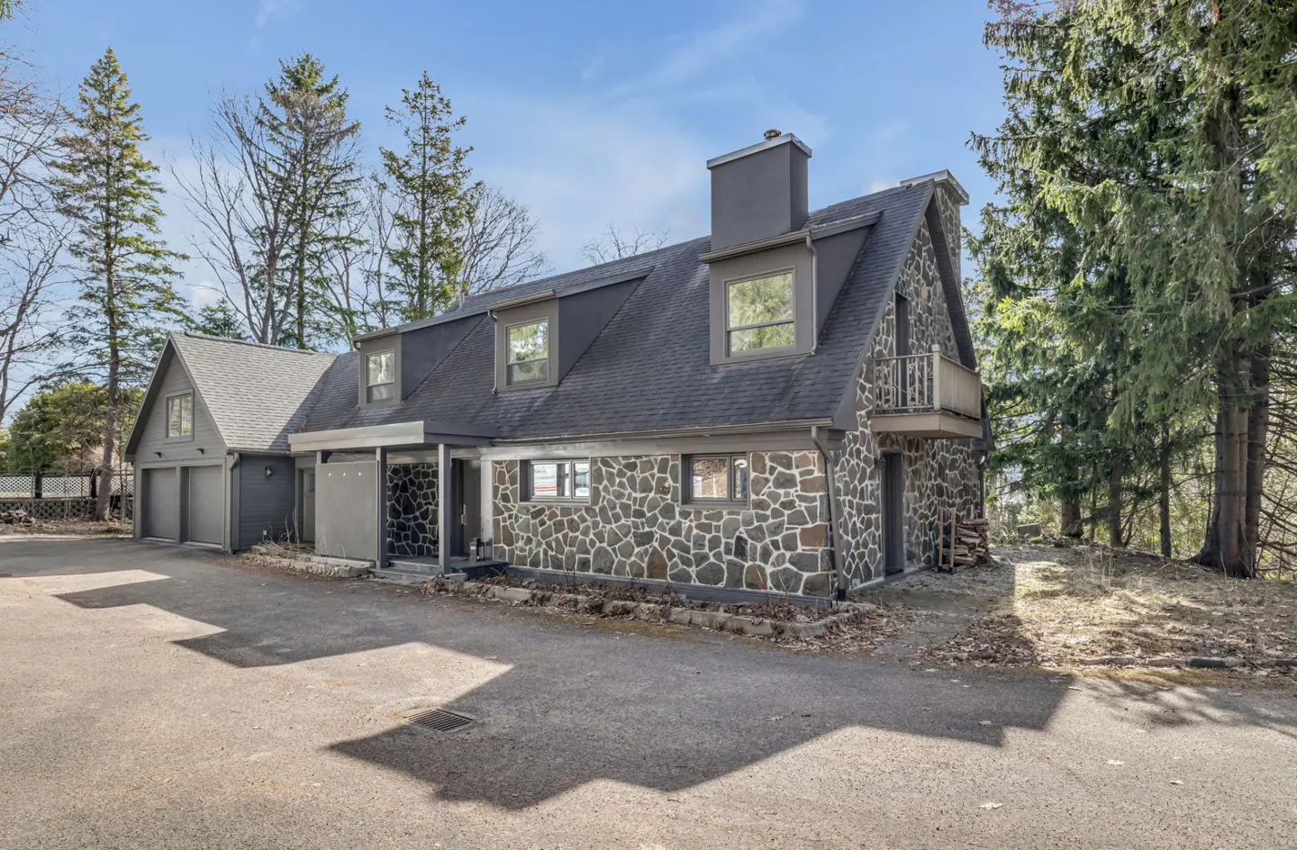Exterior view of a two-story house with stone walls, a gray roof, and a two-car garage on a paved driveway.
