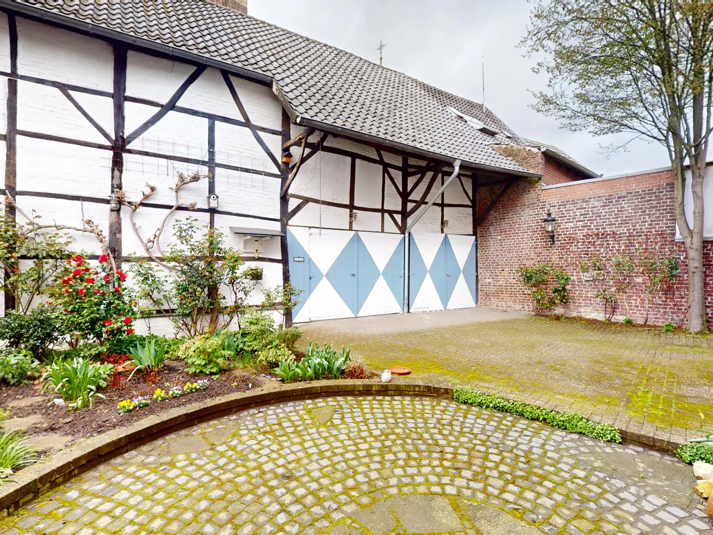 Exterior view of a half-timbered house with blue and white diamond patterned doors, a brick wall, and a cobblestone courtyard.