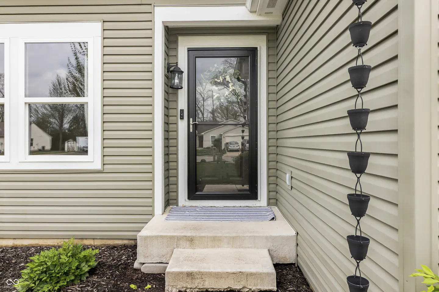 Front exterior of a home with light green siding, a black-framed glass door, and a rain chain.