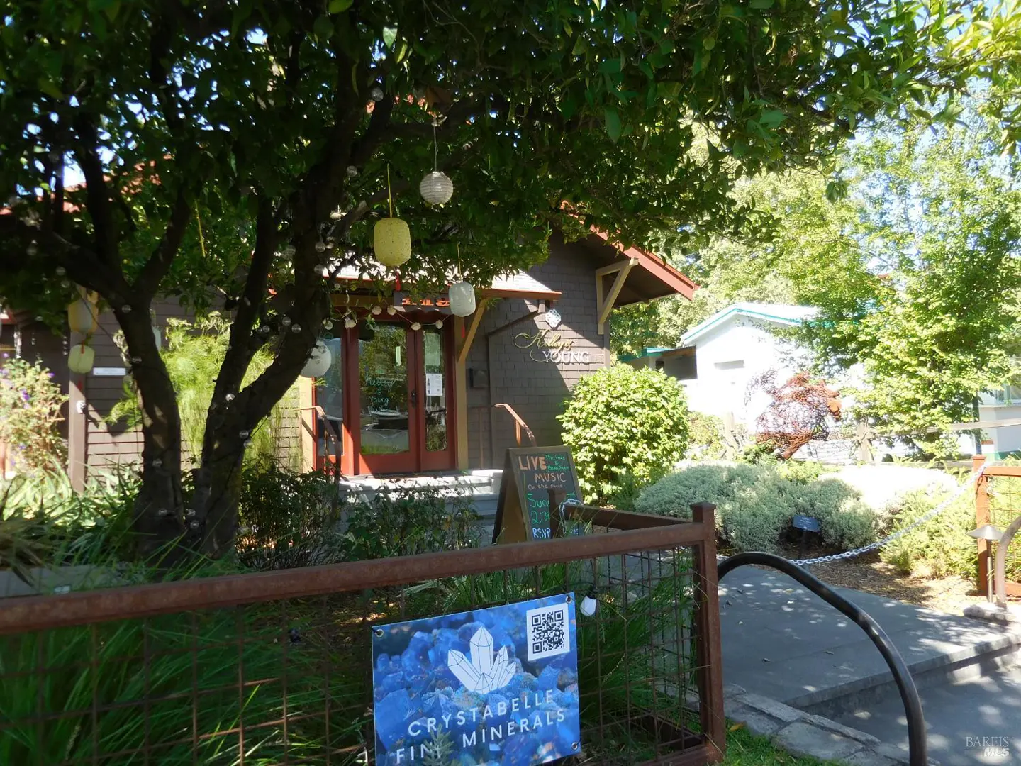 Exterior view of a shop with red doors, a sign for "Crystabelle Fine Minerals", and paper lanterns hanging from a tree.