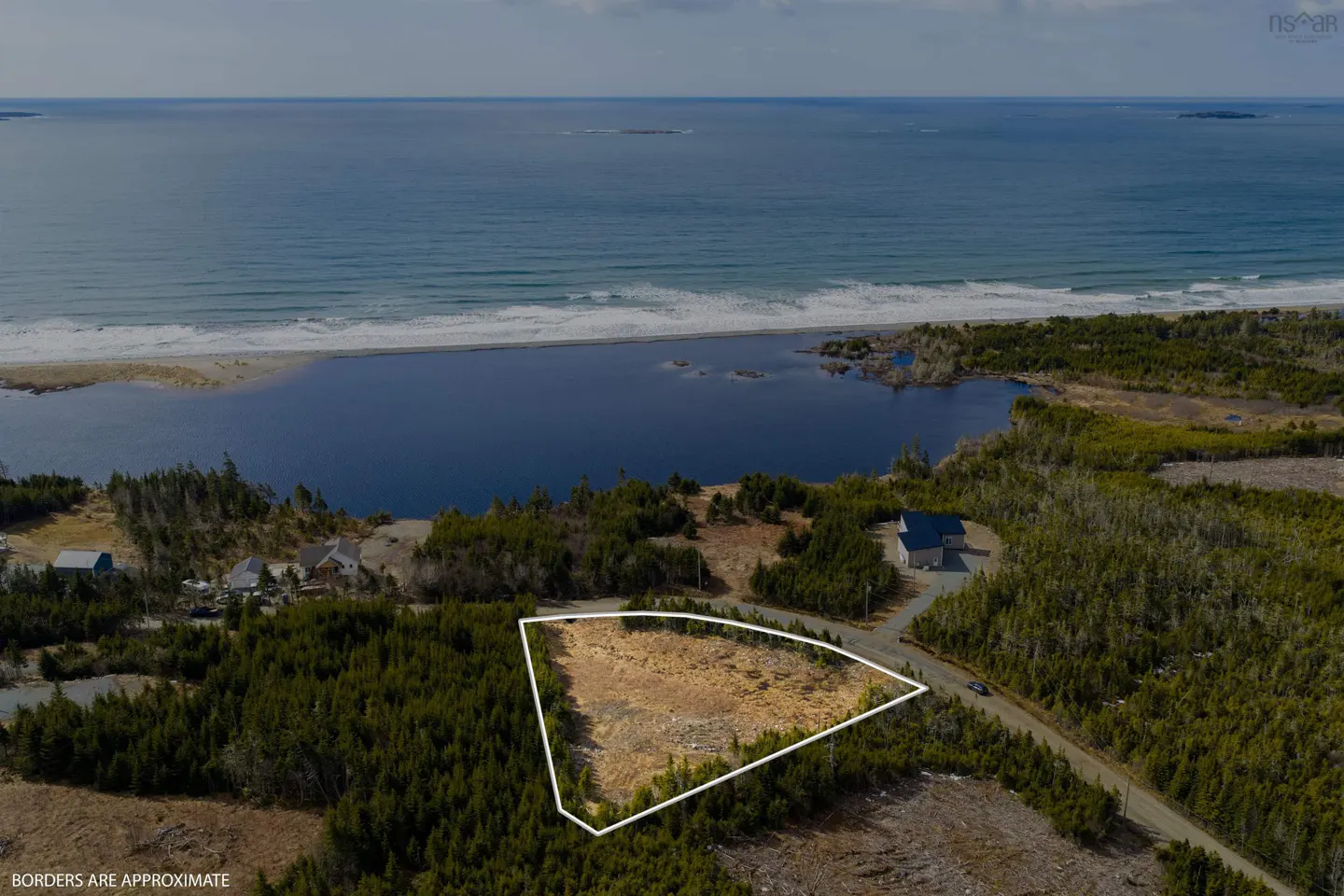 Aerial view of a vacant lot outlined in white, near a lake and the ocean. Trees surround the lot.