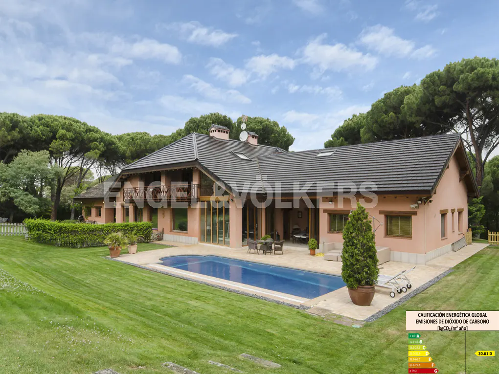 Exterior view of a salmon-colored house with a pool, green lawn, and trees under a blue sky.