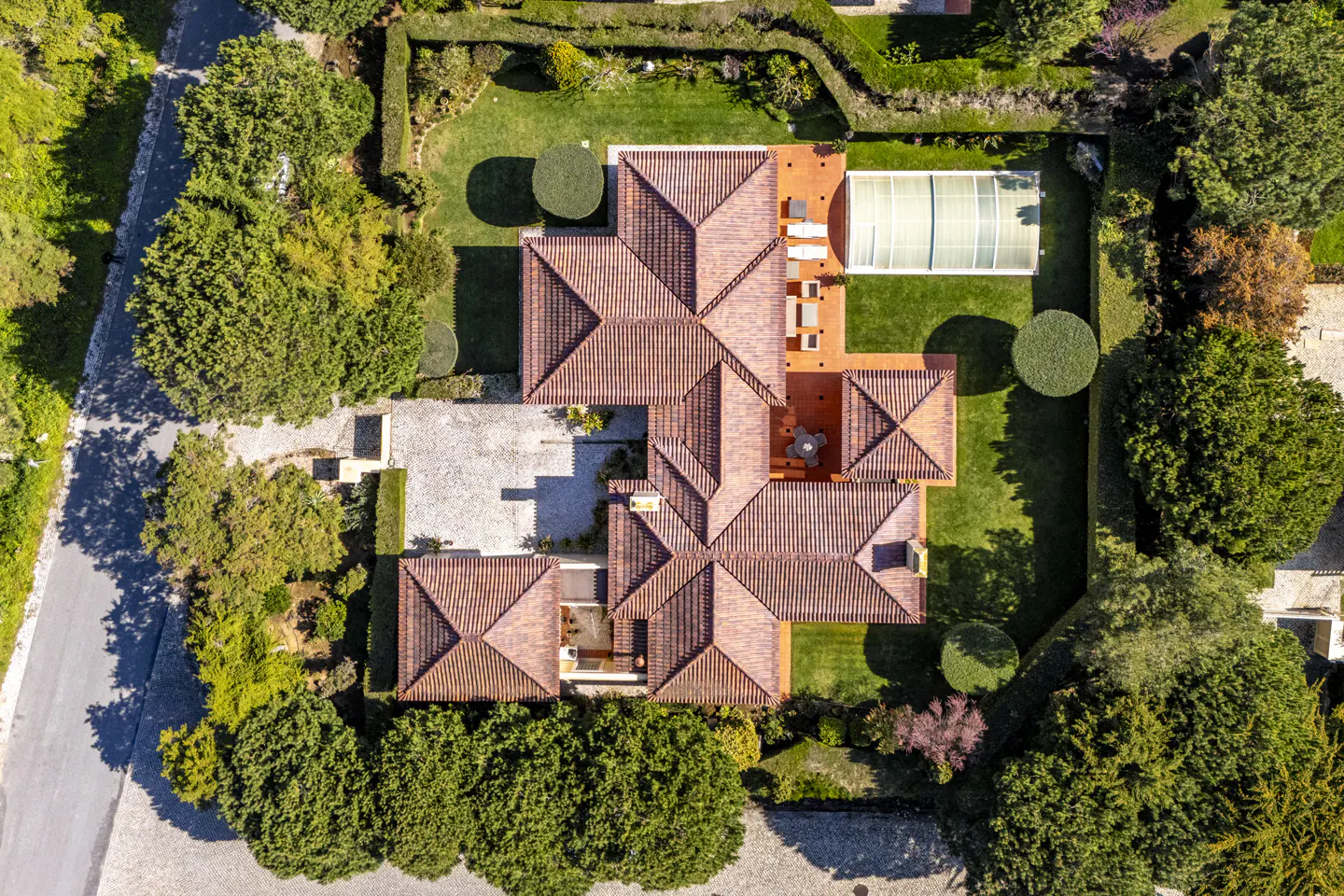Aerial view of a large home with a red tile roof, green lawn, pool, and manicured hedges.