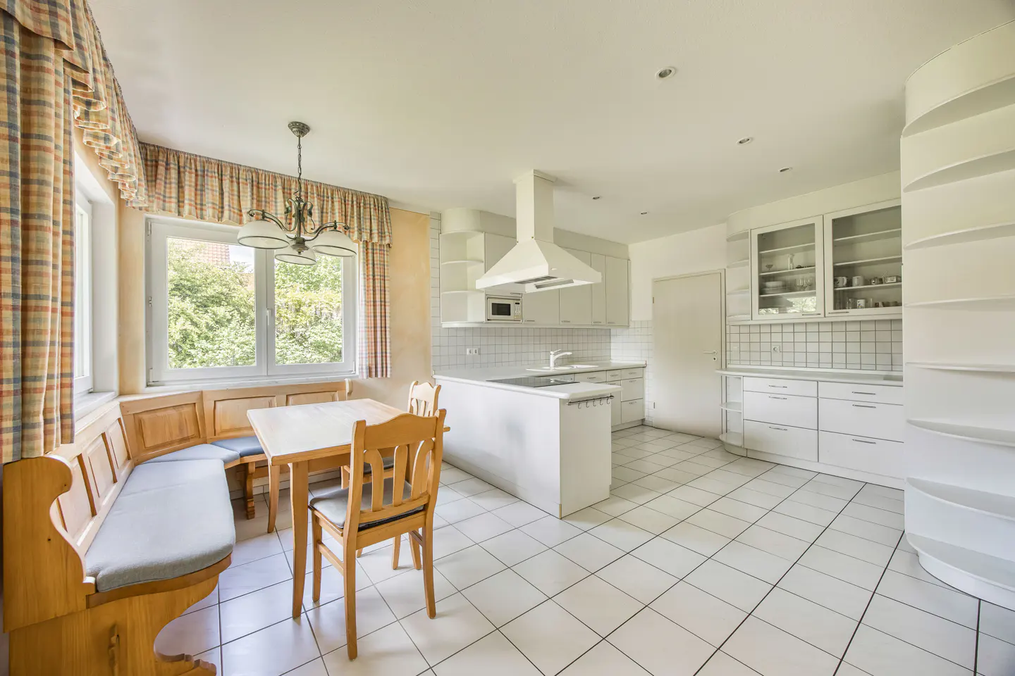 Bright kitchen with white cabinets, tiled floor, and a wooden dining nook with a table and chairs by a window.
