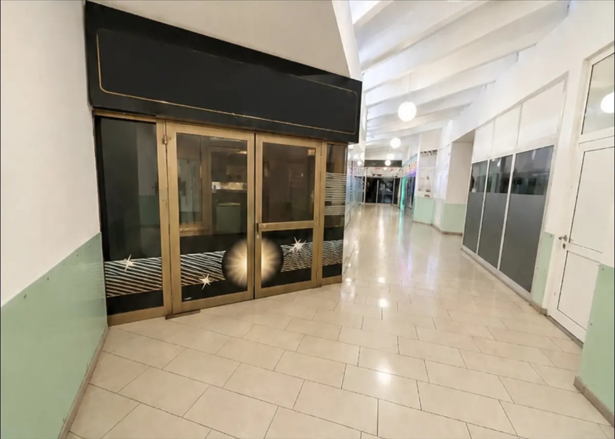 A commercial space with gold-framed glass doors and a black sign, located in a long hallway with tiled floors.