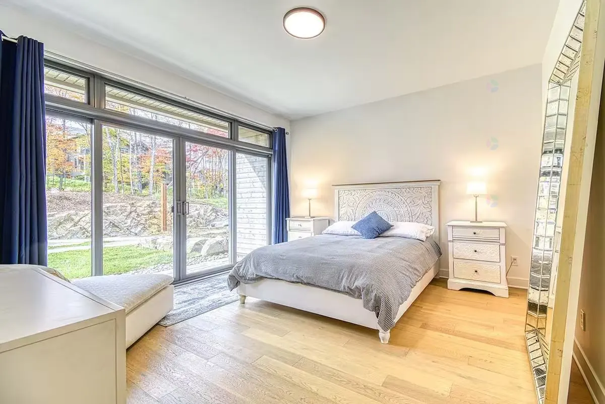 Bedroom with light wood floors, white walls, and a large sliding glass door to a yard with fall foliage.