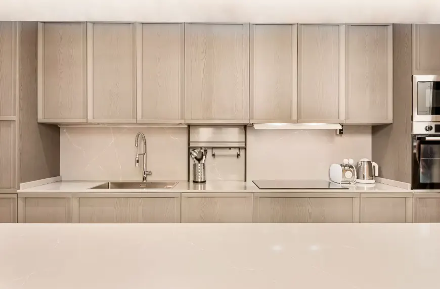 Modern kitchen with light wood cabinets, stainless steel sink, and appliances. A white countertop is in the foreground.