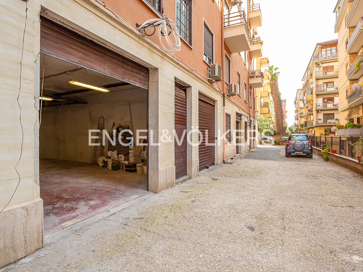 Exterior view of a garage with an open brown door, paint cans inside, and a car parked on the street.