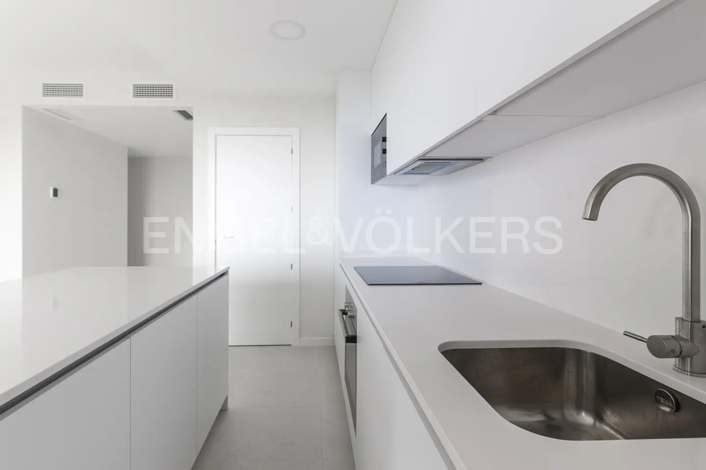 A bright, modern kitchen with white cabinets, countertops, and walls. A stainless steel sink and faucet are visible.