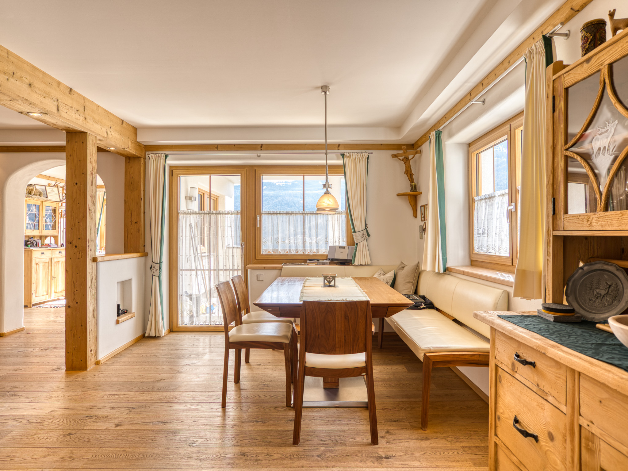 Rustic dining area with wooden table, chairs, and bench seating, featuring light wood floors and mountain views.