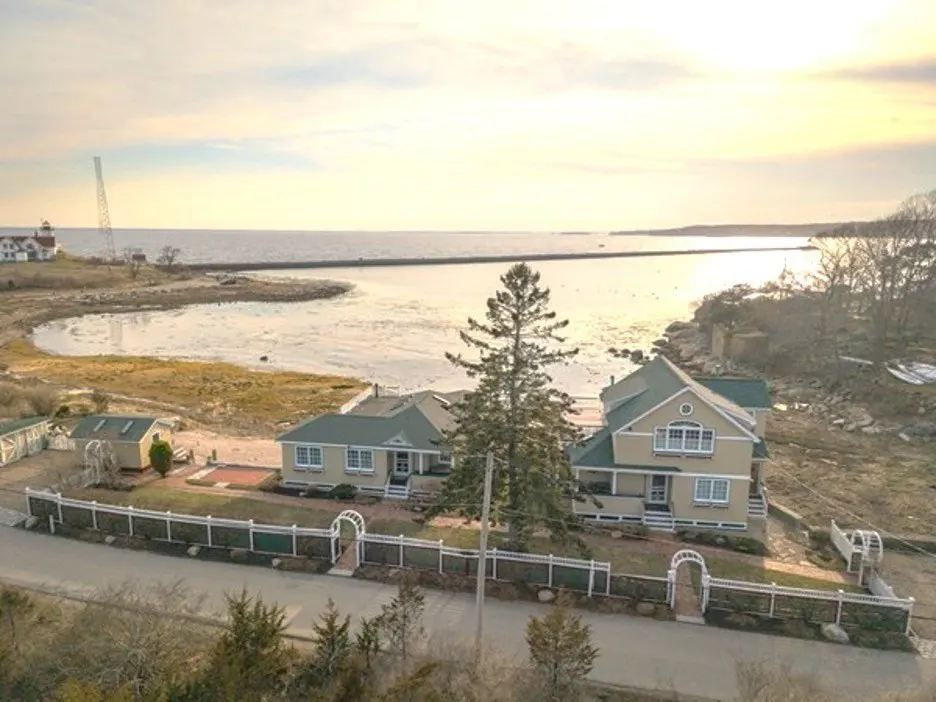 Aerial view of tan houses with green roofs, white fences, and ocean backdrop at sunset.