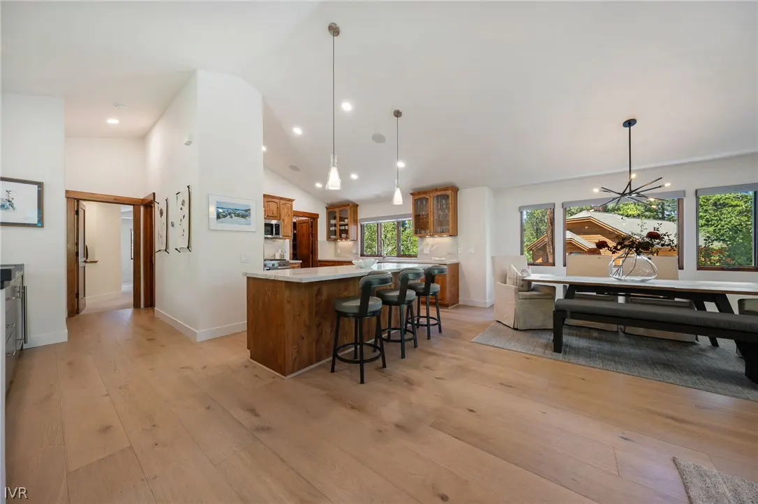 A bright, open-concept kitchen and dining area with wood floors, a kitchen island with bar stools, and a dining table with a bench.