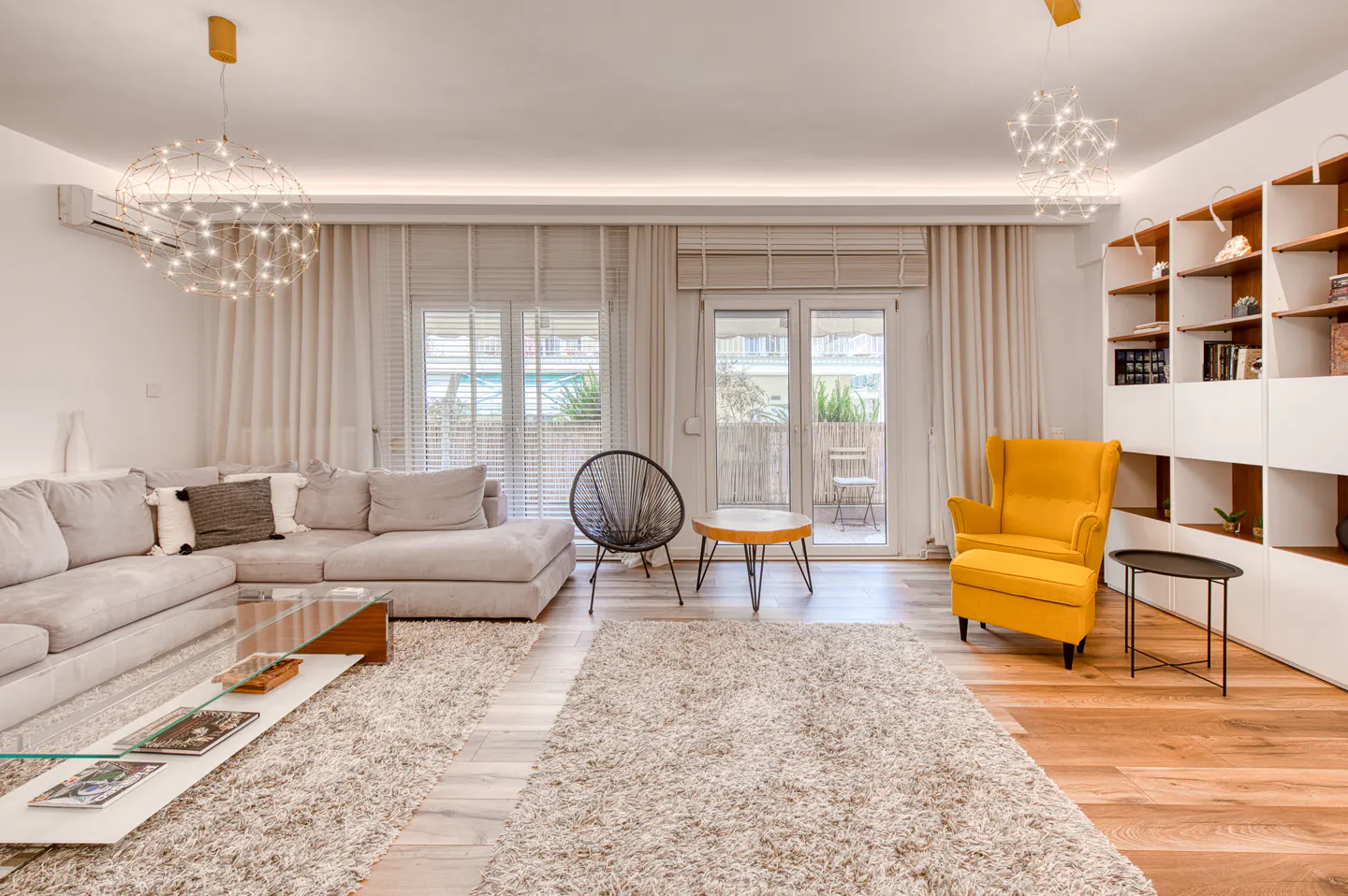 Modern living room with a grey sectional sofa, bright yellow armchair, glass coffee table, and large shaggy area rugs.