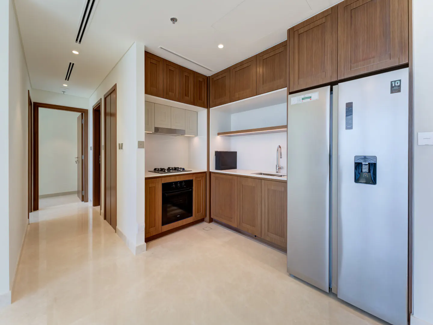 A modern kitchen with wood cabinets, stainless steel appliances, and a hallway leading to other rooms.
