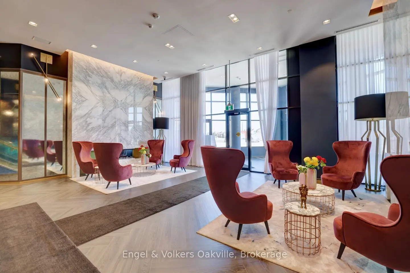 Lobby area with red armchairs, marble wall, and floor-to-ceiling windows. Tables with flowers sit between the chairs.