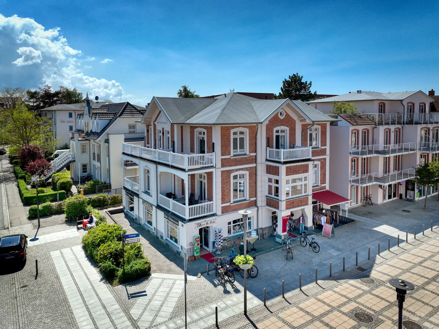 Aerial view of a three-story brick building with white balconies, a shop front, and bicycles parked outside on a sunny day.