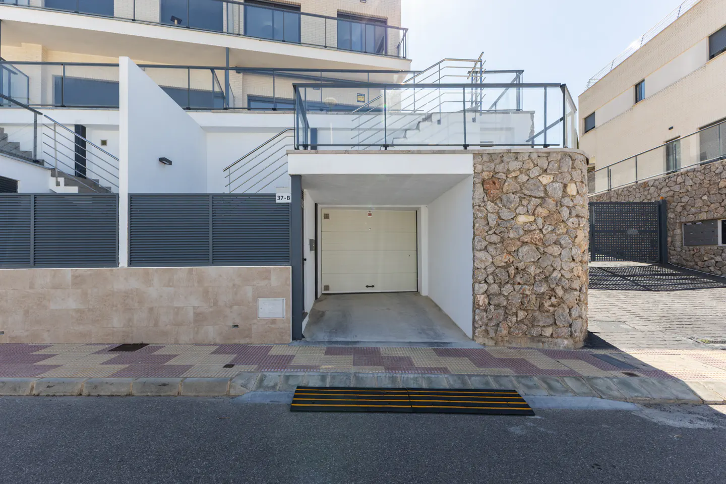 Exterior view of a modern white house with an open garage, stone accents, and gray metal fencing.