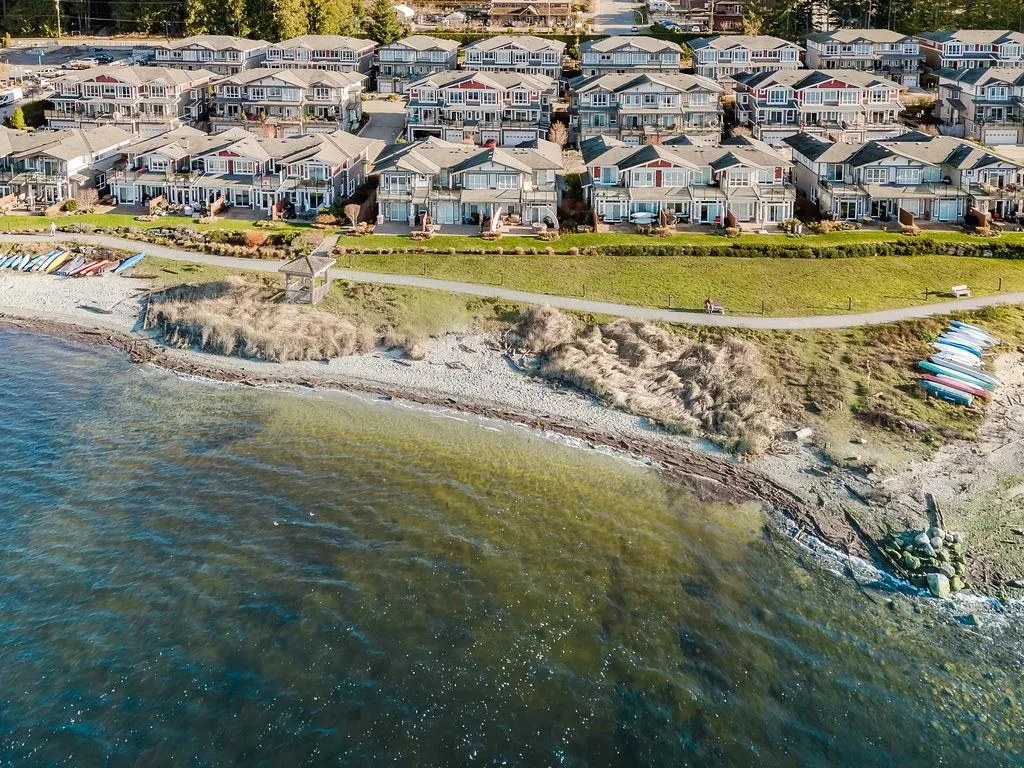 Aerial view of waterfront homes with a beach, path, and kayaks. The water is blue-green.