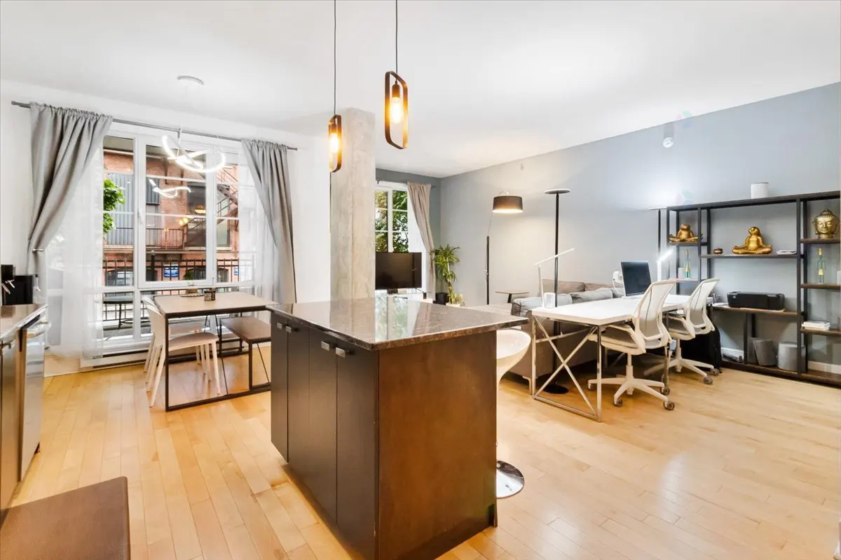 Open-concept apartment with wood floors, a kitchen island, dining table, and a work area with desks and chairs.