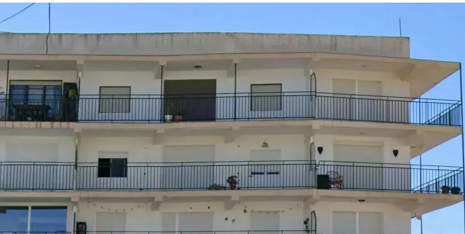 Exterior view of a multi-story white apartment building with black metal railings on each balcony against a blue sky.