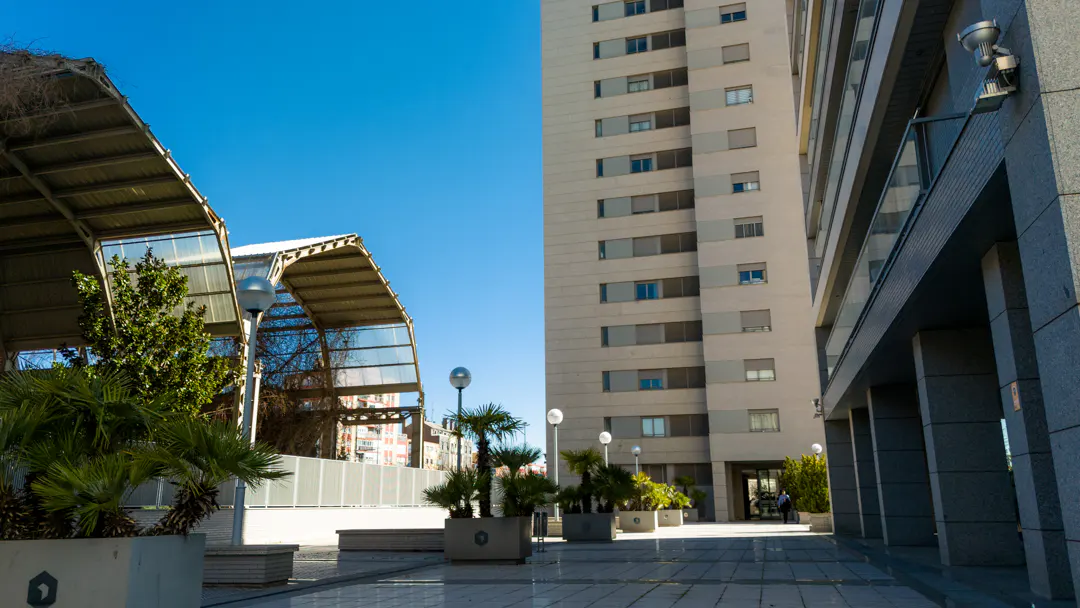 Exterior view of a modern building with a covered walkway, palm trees, and a clear blue sky.