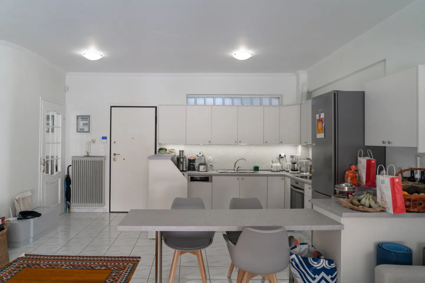 Modern kitchen with white cabinets, grey countertops, stainless steel appliances, and a dining table with grey chairs.