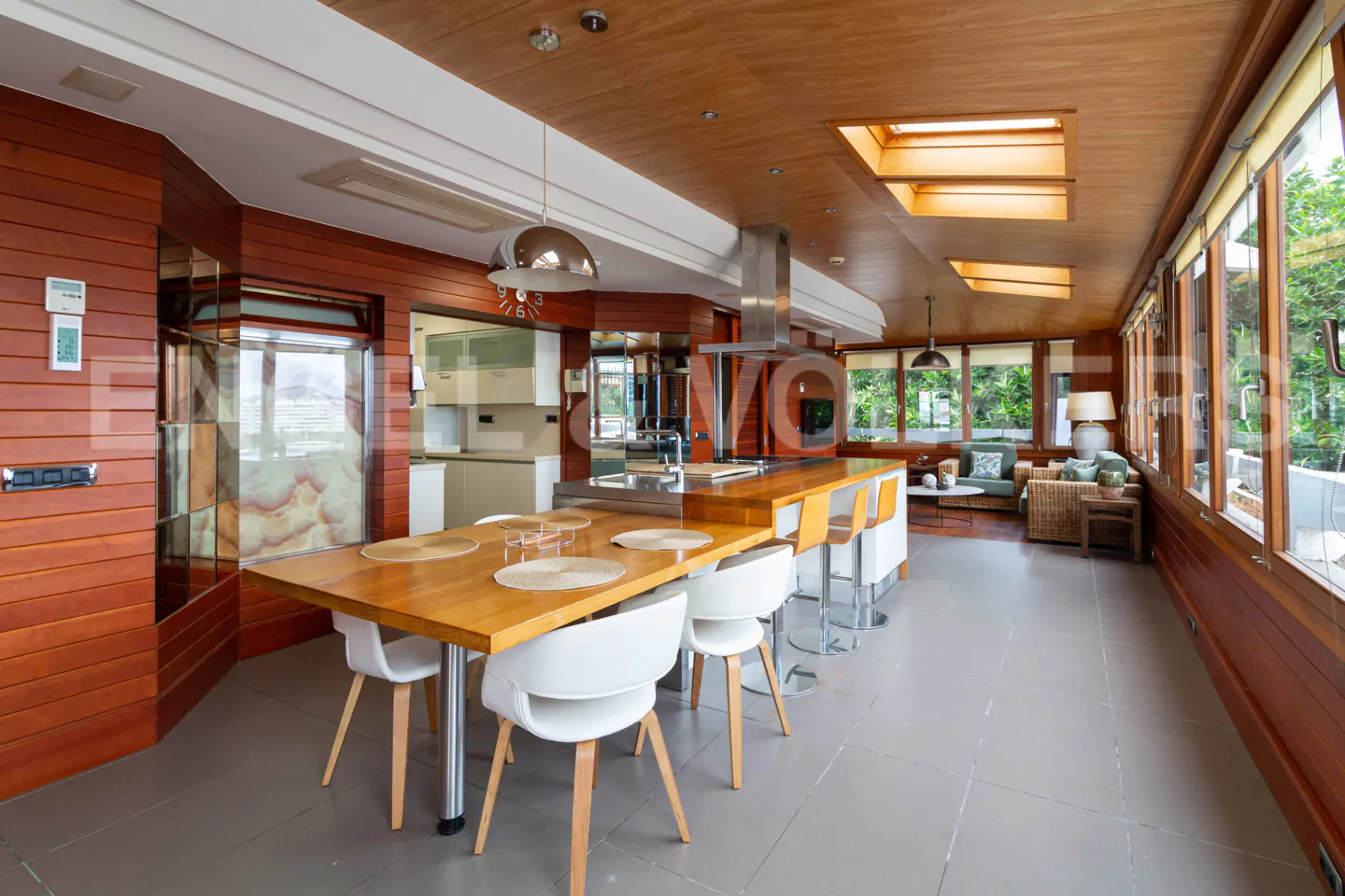A spacious kitchen with wood paneling, a large wooden table with white chairs, and a kitchen island with bar stools.