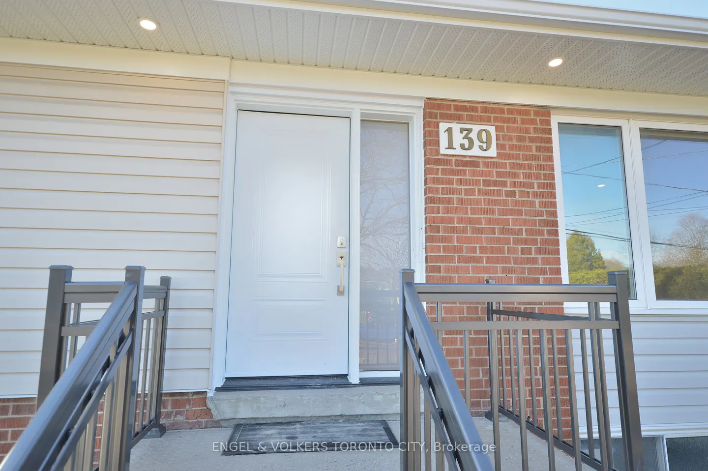 Exterior shot of a home's entrance with a white door, brick wall with "139" address, and black railings.