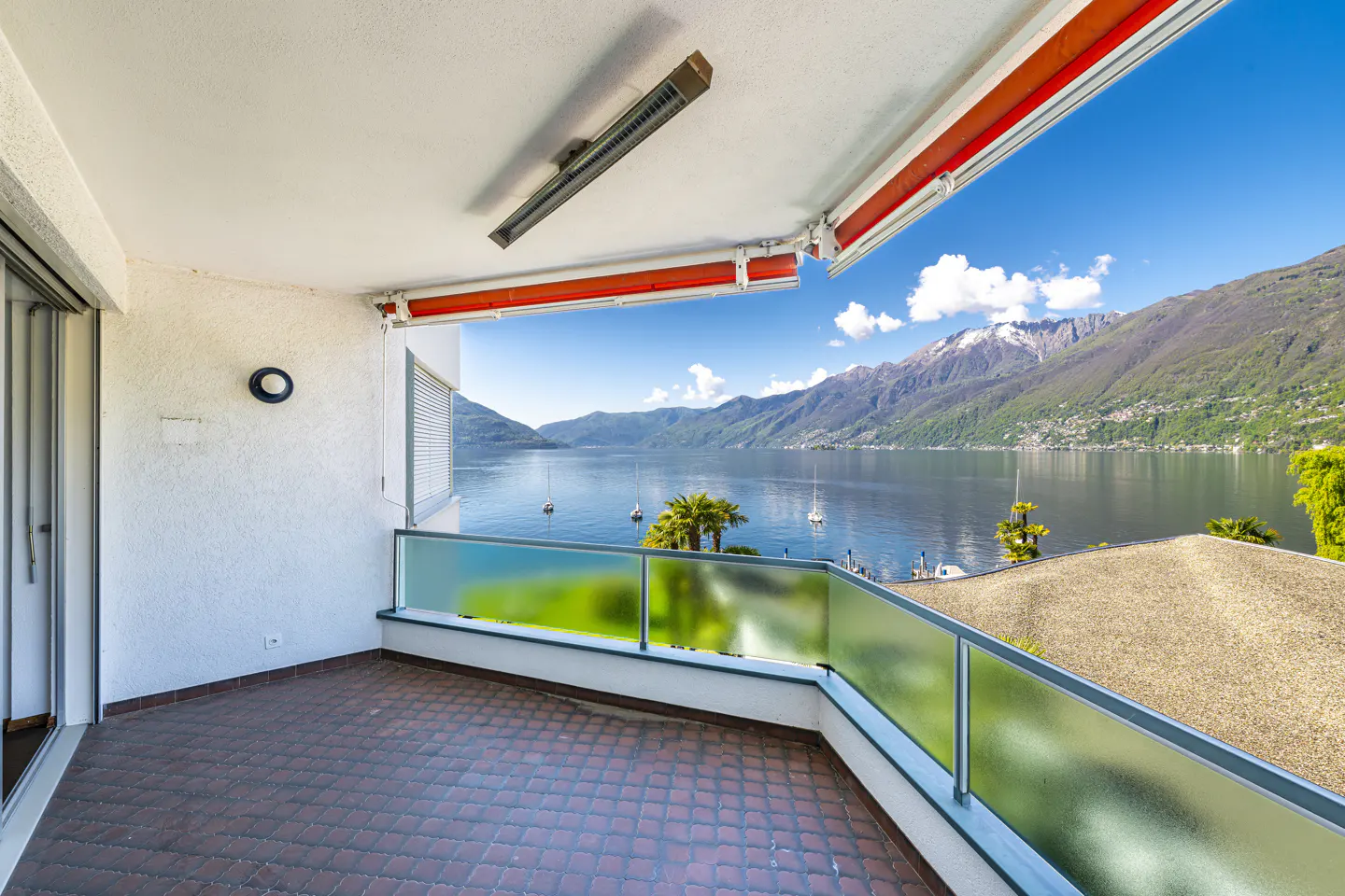 Balcony view of a lake and mountains. The balcony has a red brick floor and a glass railing.