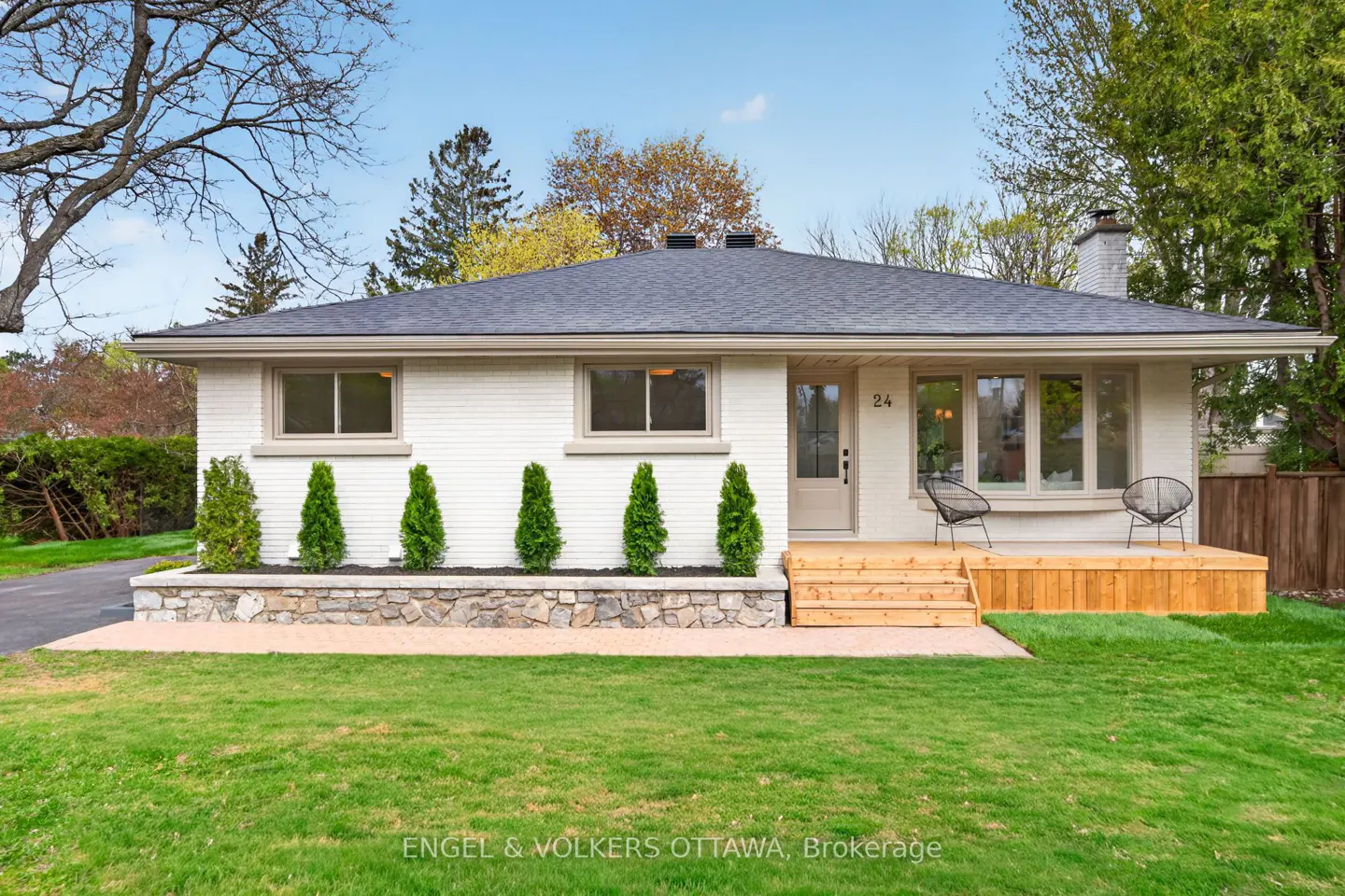 Exterior of a white brick house with a gray roof, a wooden porch, and green lawn.
