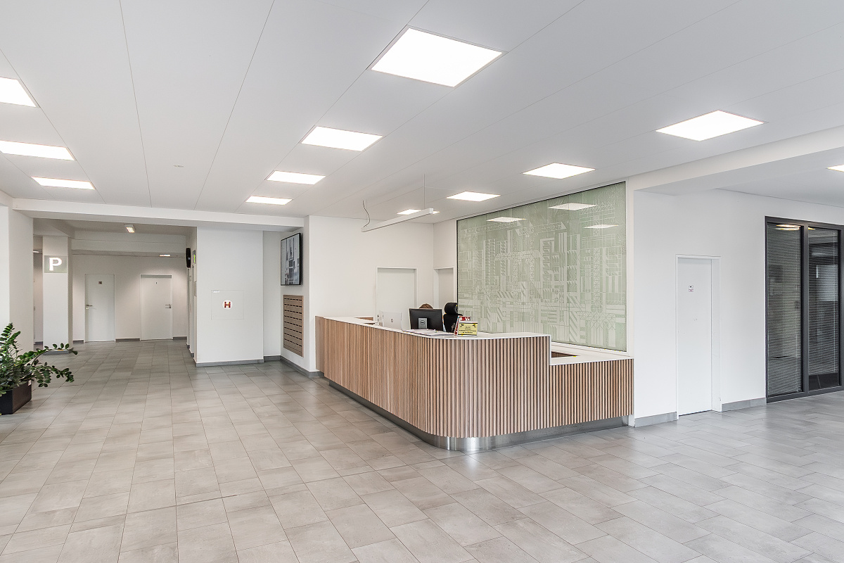 Modern office lobby with a light wood reception desk, gray tiled floors, white walls, and bright recessed ceiling lights. [AI-generated text]