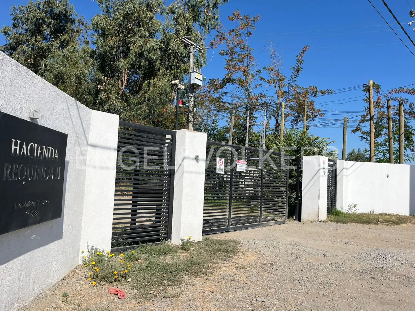 Entrance to Hacienda Requinoa with black metal gates and white walls under a blue sky.