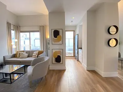 Living room with a gray sofa, chair, and coffee table. Two abstract paintings hang on the wall. Hardwood floors run throughout the space.