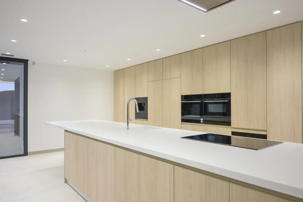 Modern kitchen with light wood cabinets, white countertop island, stainless steel faucet, and built-in black appliances.
