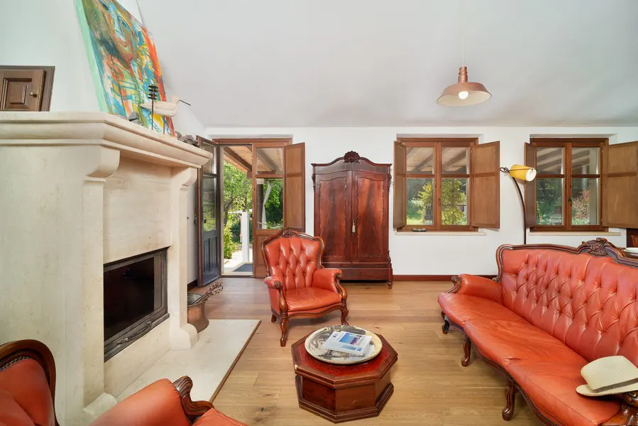 Bright living room with a stone fireplace, red leather furniture, wood floors, and an open door to a garden.