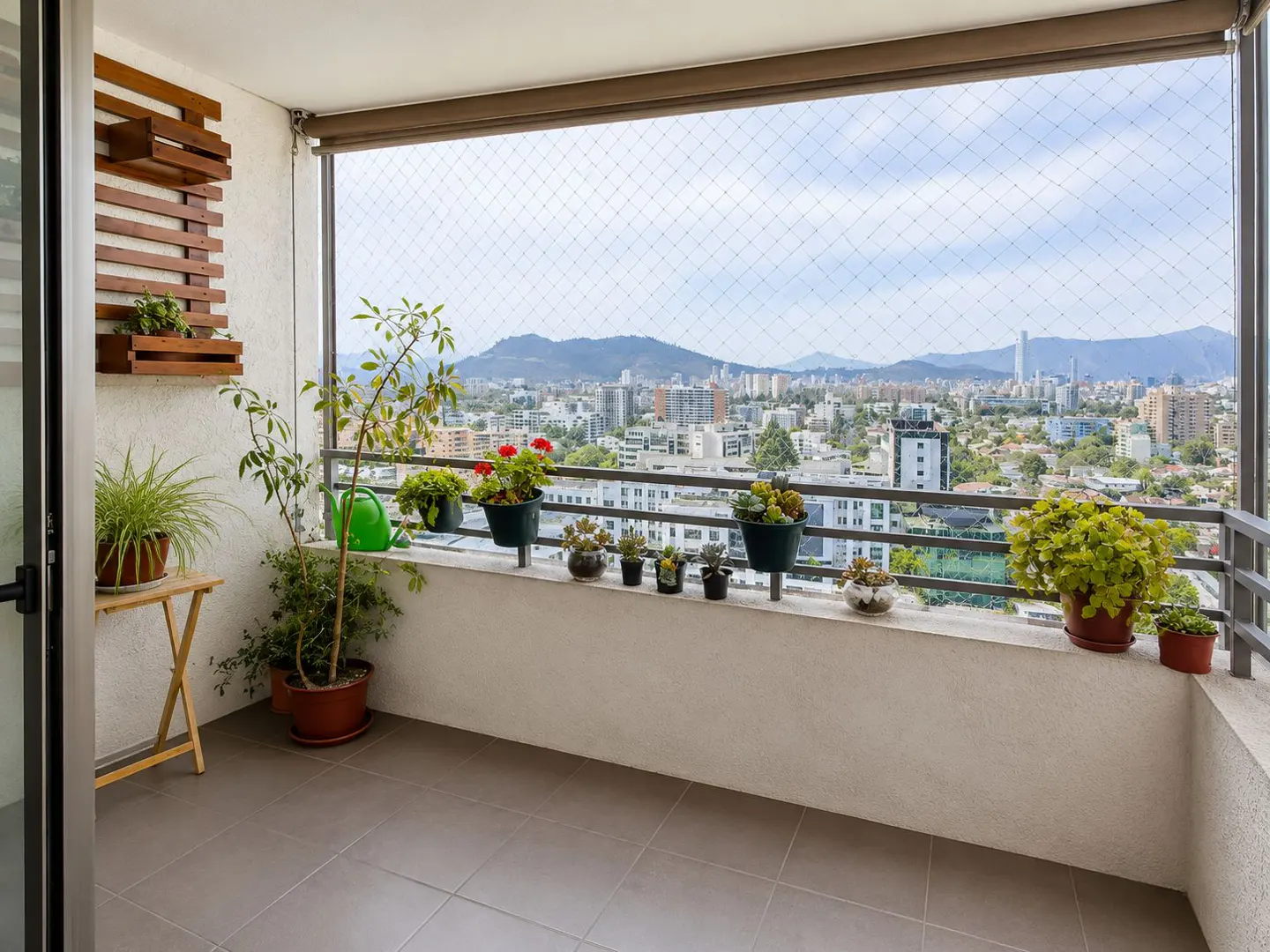Balcony with potted plants, wood shelf, and city view. Gray tile floor and safety net.