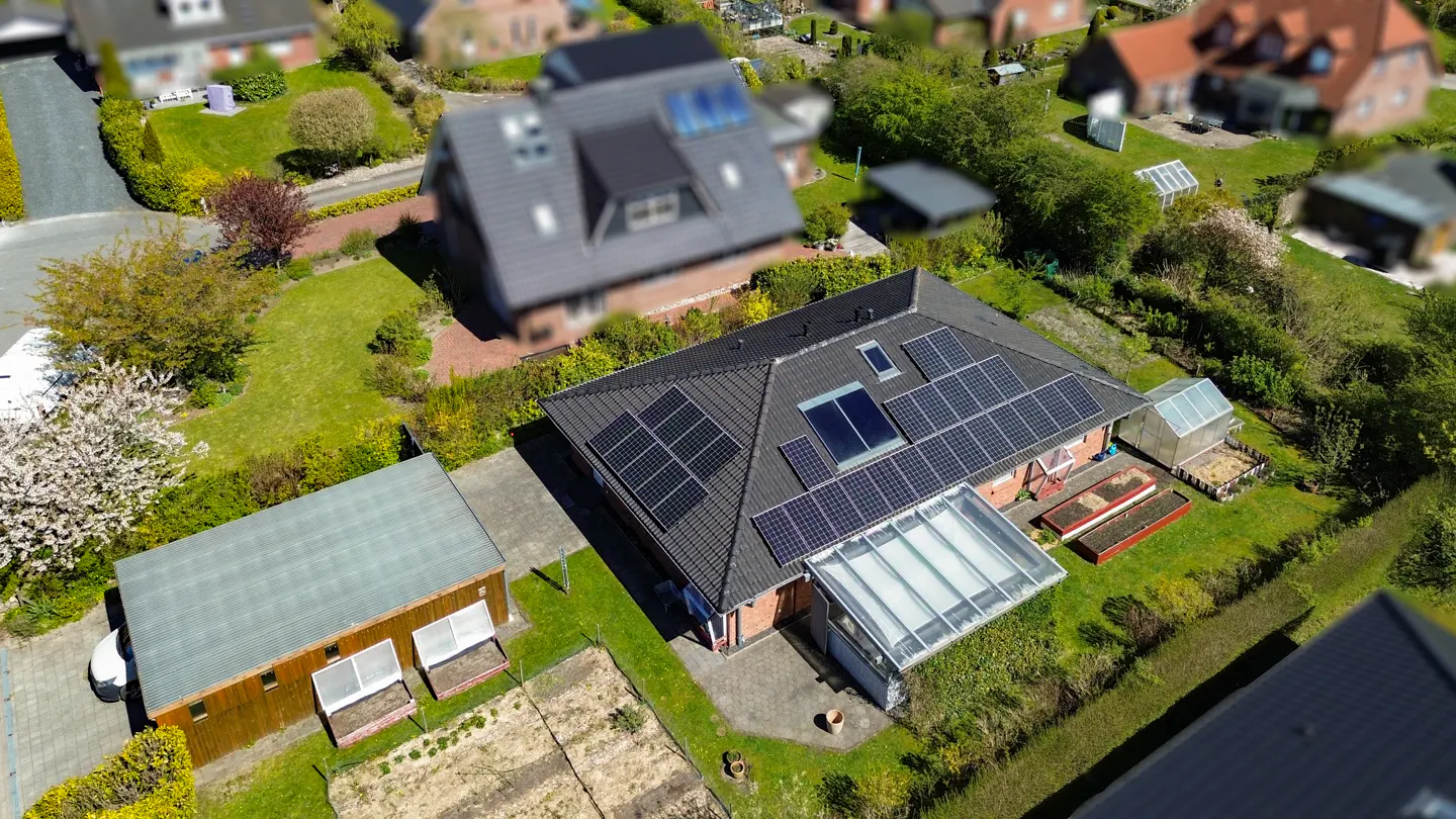 Aerial view of a house with solar panels on a dark roof, a glass conservatory, and a garden with a shed.