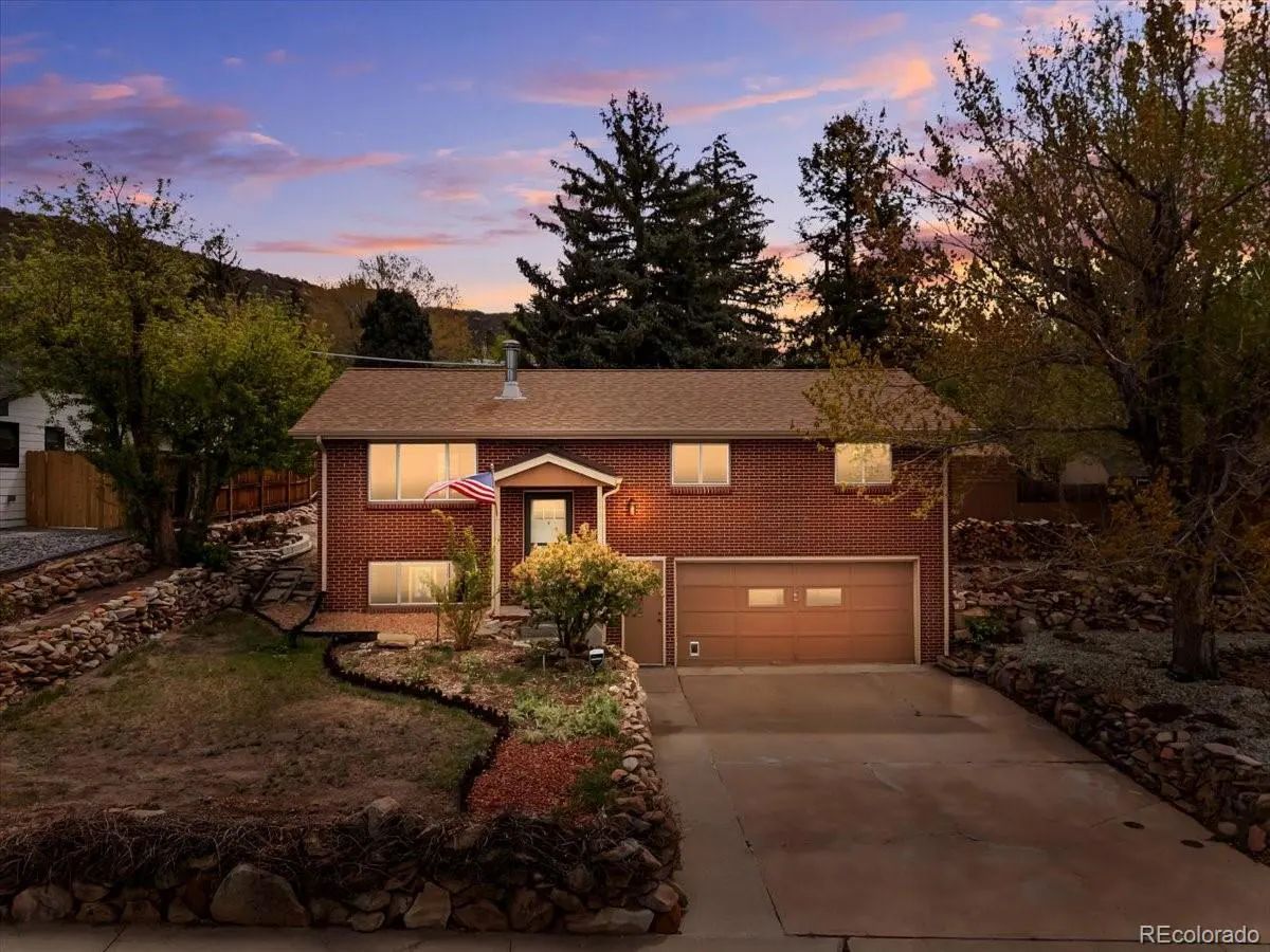 Brick house with brown roof and two-car garage. An American flag is displayed near the front door. Trees surround the property.
