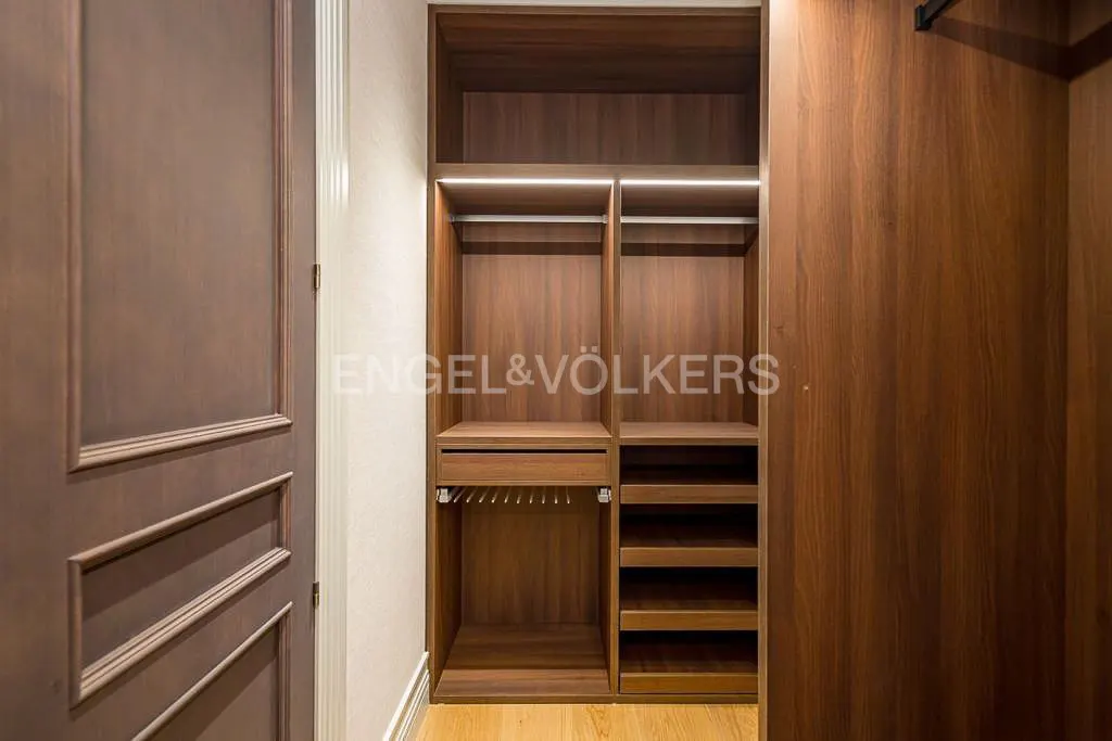 A walk-in closet with wood shelves, hanging rods, and a pull-out rack. A closed wood door is on the left.