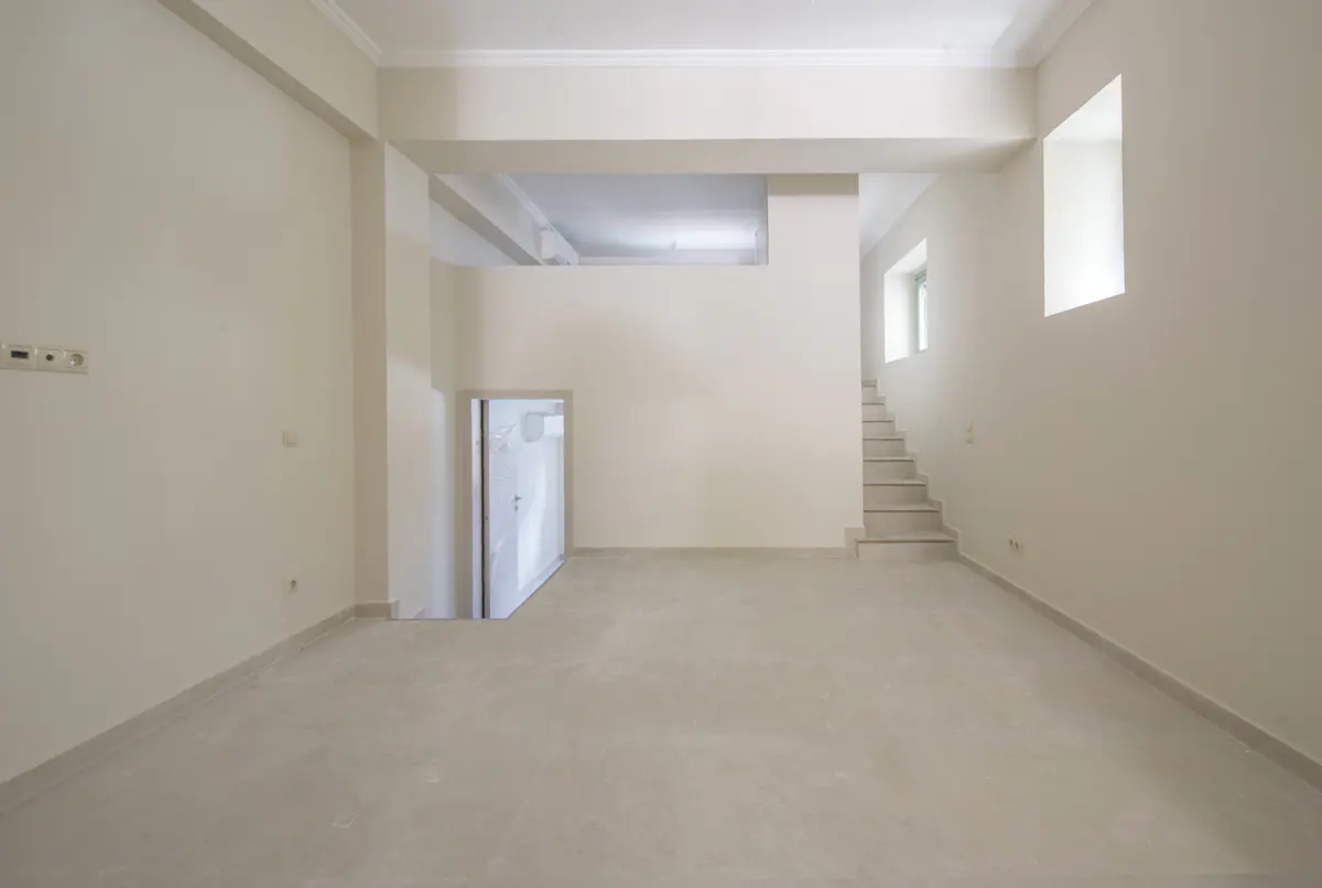 Empty room with beige walls, a white door, and stairs leading up to a window.
