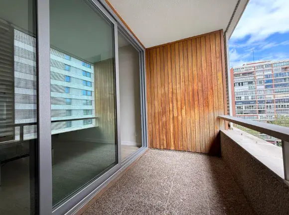 A balcony with wood paneling and a view of a building through a sliding glass door.