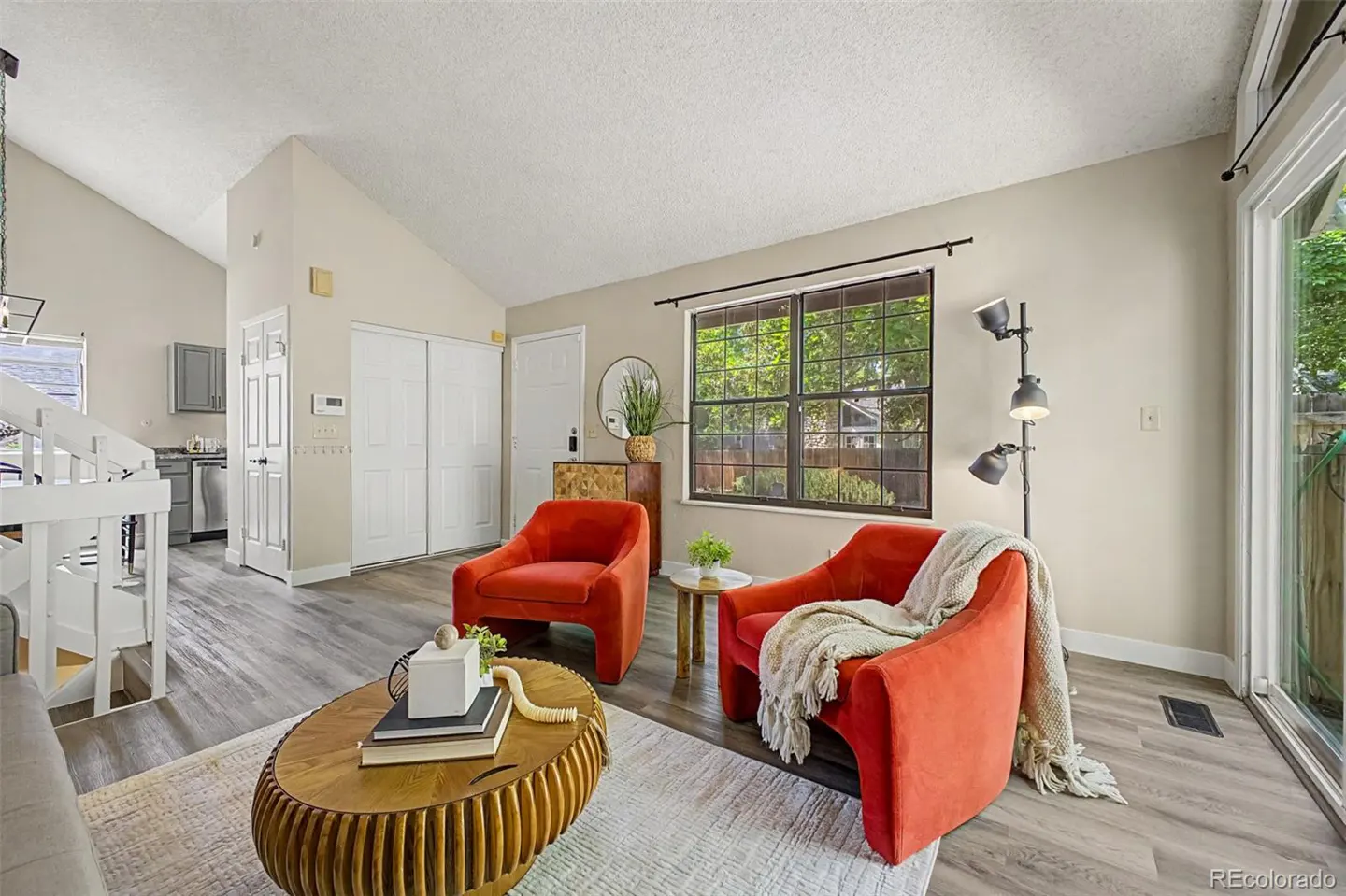 Bright living room with two orange armchairs, a wooden coffee table, and a floor lamp on light wood-look flooring.