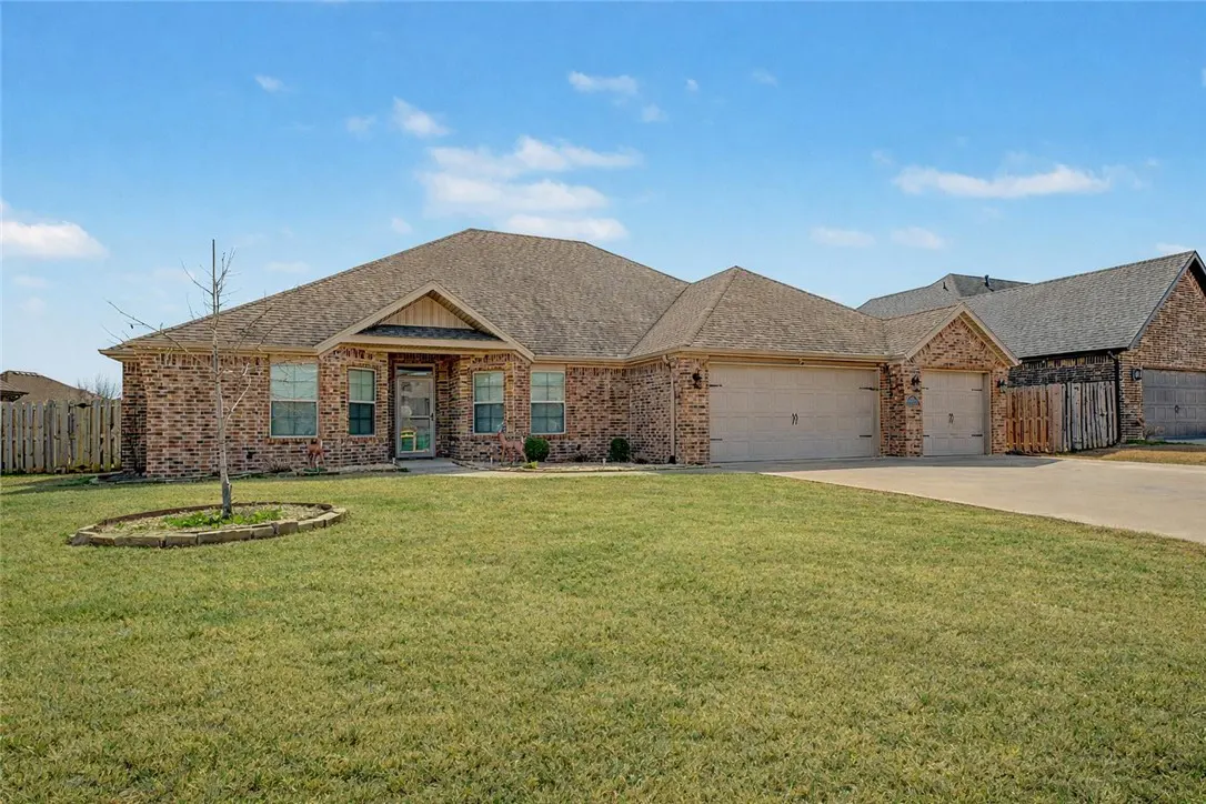 A single-story brick house with a brown roof and a two-car garage on a green lawn under a blue sky.