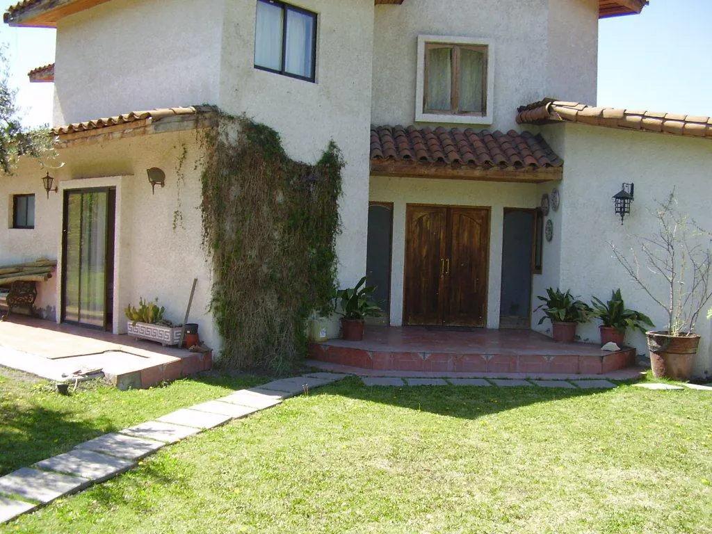 Two-story stucco house with a red tile roof, brown double doors, and a stone walkway leading to the front entrance. Green lawn and plants.
