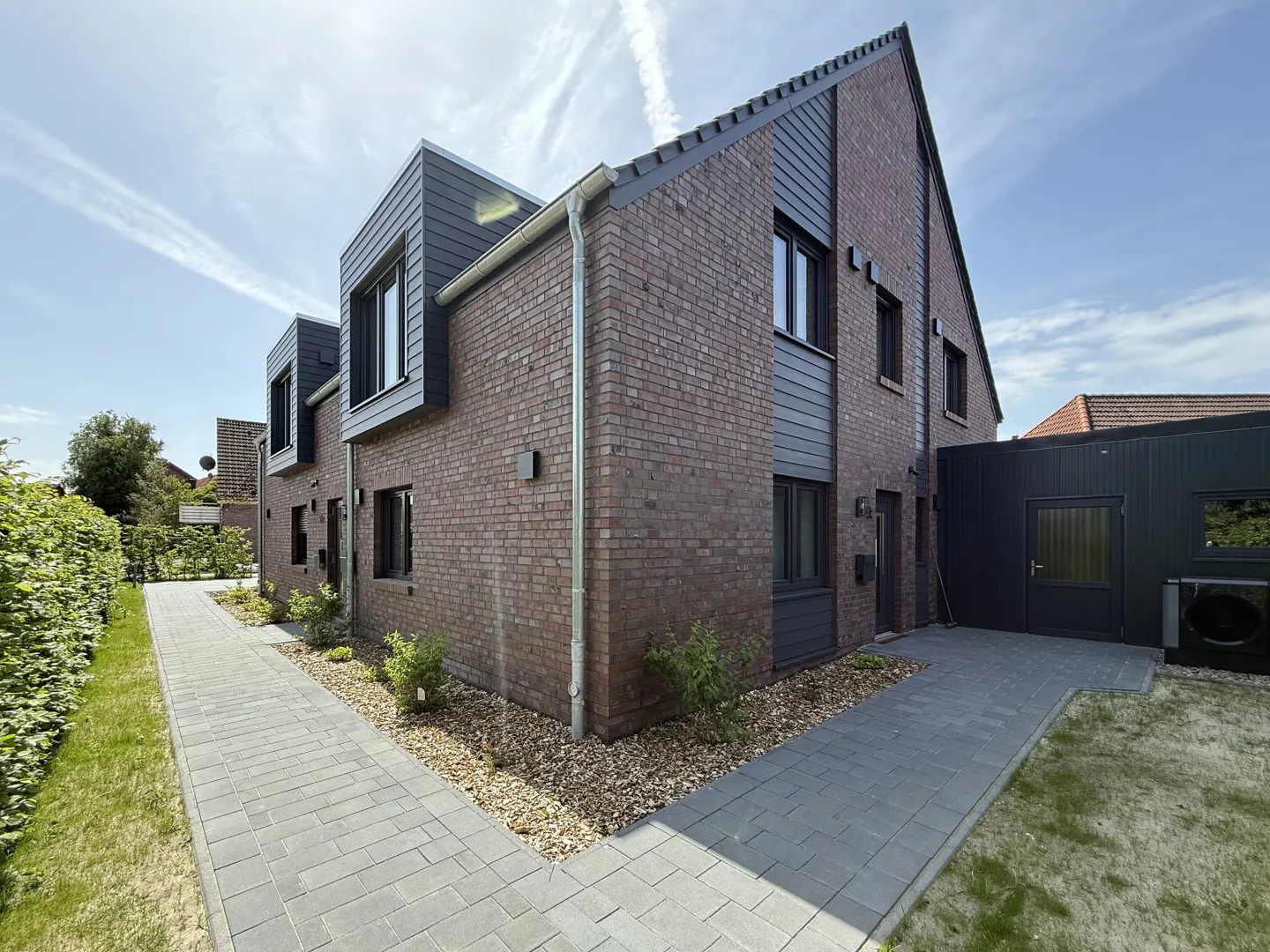 Exterior view of a two-story brick house with gray siding and black-framed windows, a gray brick walkway, and green grass.