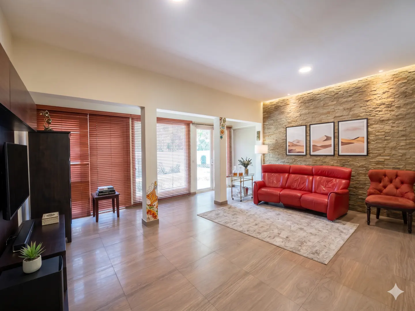 A spacious living room with a red leather sofa, stone accent wall, and wood-look tile flooring.